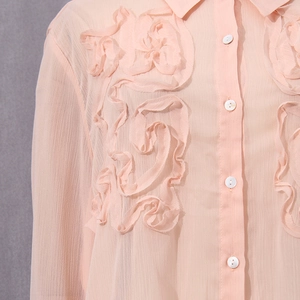 Detail of pink chiffon shirt featuring a large 3D floral applique and pleated fabric texture