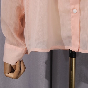Detail of peach chiffon shirt featuring white buttons and vertical stripe texture