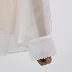 Détail d'un chemisier blanc à manches longues en tissu texturé et poignets larges