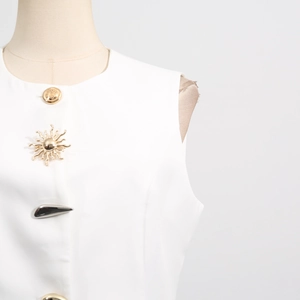 Detail of white sleeveless vest featuring unique gold and silver decorative metal buttons