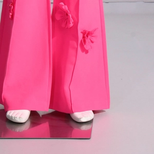 Dettaglio dei pantaloni a zampa rosa con applicazioni floreali 3D e tessuto a trama fitta