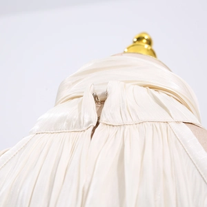 Close-up of metal hook closure on pleated cream blouse with satin finish texture