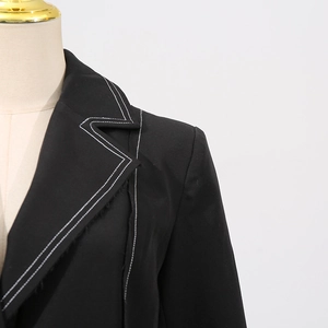 Detail of black trench coat featuring white contrast stitching and deconstructed frayed lapel