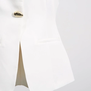 Detailed close-up of white vest with gold teardrop button and slit hem detail