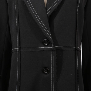 Detail shot of black trench coat with white contrast stitching and frayed edge design