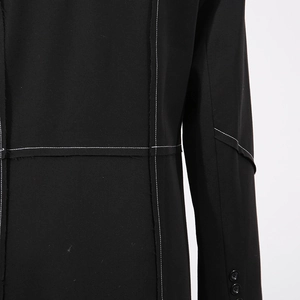 Detail view of black trench coat sleeve featuring white contrast stitching and buttons