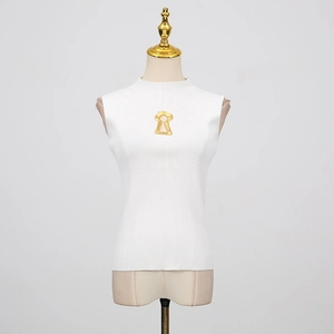 Détail d'un haut en maille blanc sans manches avec col montant et bijou en métal doré