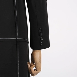 Detail of black long coat featuring white contrast stitching and four-button cuffs