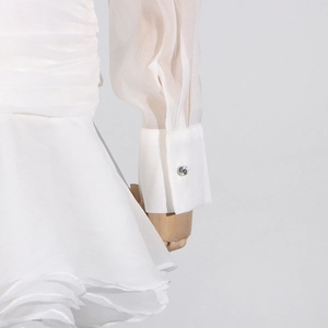 Detailed view of white pleated chiffon dress sleeve with sparkling rhinestone cuff button