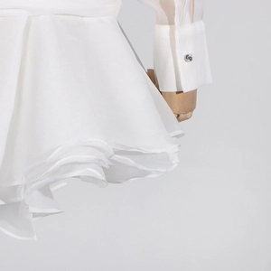 Detail of white dress showing layered ruffle hem and buttoned sleeve cuffs