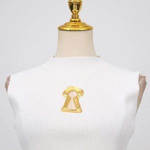 Détail du gilet en maille côtelée blanche avec élément décoratif en métal doré chic