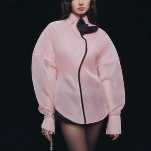 Detail of pink sheer puff sleeve shirt with a large black contrast bow and edging