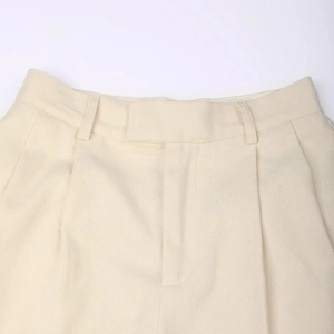 Detail of high-waist beige trousers showing waist pleats and premium twill fabric texture