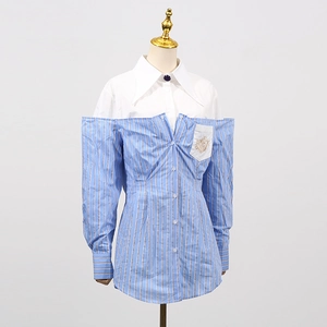 Dettaglio camicia a righe blu con stemma ricamato in oro su una tasca bianca