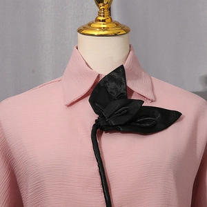 Detail of pink crinkled shirt featuring a large 3D black flower on the collar