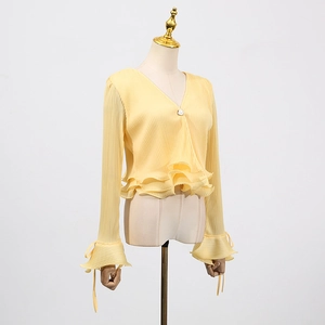 Detail of light yellow pleated cardigan with pearl button and ruffled cuffs