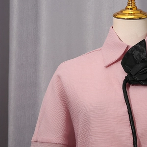 Detail of pink textured shirt featuring a large black fabric flower on the lapel
