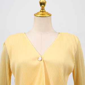 Detail of light yellow knit cardigan featuring vertical pleats and decorative square button