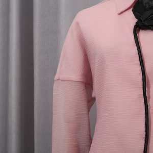 Detail view of pink textured fabric on a women blouse with black floral neckline accent