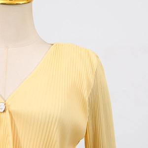 Detail of light yellow pleated top with elegant V-neck and delicate button closure