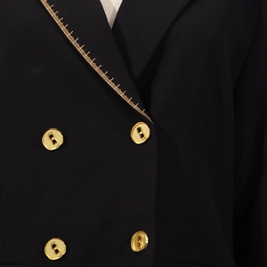 Detailaufnahme von schwarzem Blazer mit goldenem Linealmuster am Revers und verzierten Knöpfen