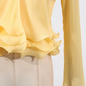 Detail view of the elegant yellow pleated fabric and ruffled hemline of this knit cardigan