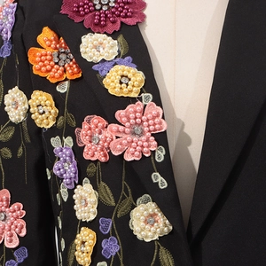 Détail de la broderie florale 3D colorée avec perles sur une veste noire chic