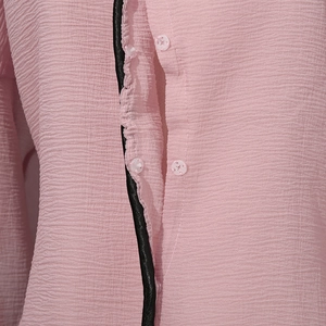 Detail of pink pleated shirt fabric with round buttons and contrasting black trim