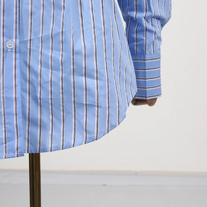 Dettaglio camicia a righe azzurre con orlo curvo e bottoni bianchi su manichino