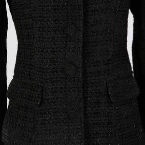 Dettaglio ravvicinato della giacca in tweed nero con bottoni rivestiti e trama ricca