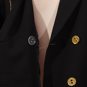 Detail eines schwarzen Blazers mit goldfarbenen Metallknöpfen und Harzverschluss