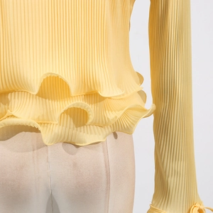Detail of light yellow pleated knit cardigan with ruffled hem and decorative sleeve ties