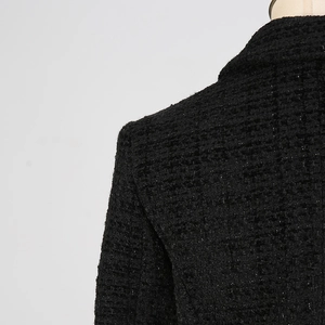 Dettaglio del blazer in tweed nero che mostra il tessuto intrecciato e il taglio spalla