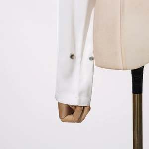 Détail des poignets d'une chemise en satin blanc avec deux boutons-pression en métal