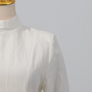 Macro shot of white high-neck dress showing pleated fabric texture and padded shoulder