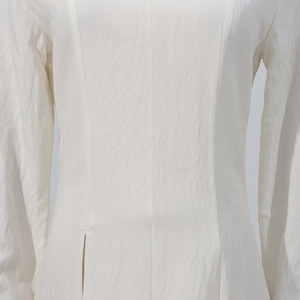 Detail view of cream white dress showing fine vertical stitching and high-slit hemline design