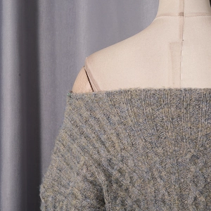 Detail of off-shoulder gray knit dress with chunky cable stitch patterns and textured fabric
