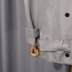 Détail du trench-coat gris montrant les boutons à double boutonnage et la ceinture à œillets