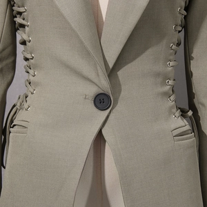 Detail of olive blazer featuring corset-style lace-up waist with silver metal eyelets
