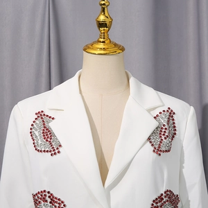 Détail d'un blazer blanc avec des motifs de lèvres en strass rouges et argentés brillants