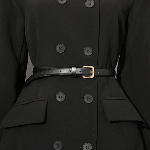 Detailed view of slim black belt with gold buckle styled on a black double-breasted coat