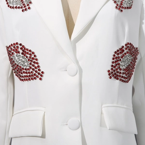 Détail de la broderie lèvres en strass brillants sur une veste de tailleur blanche