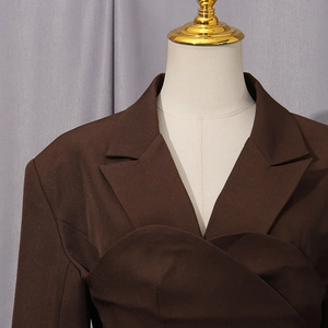 Detail of elegant dark brown suit jacket featuring unique asymmetrical pleated draping