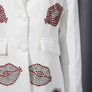 Détail de lèvres en strass rouges et argentés sur une veste de blazer blanche cintrée