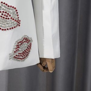 Détail de l'embellissement des lèvres en strass rouge et argent sur blazer blanc