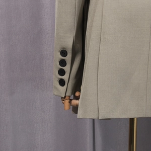 Detail of light khaki blazer cuff with four black buttons and precise pleated craftsmanship