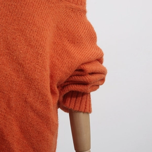 Detail of orange chunky knit sweater showing rib-knit cuffs and shoulder texture