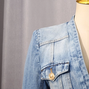 Detail of light blue denim jacket with embossed lion head gold button on chest pocket