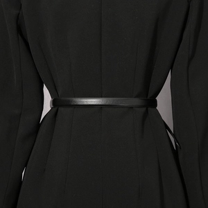 Detail shot of a slim black leather waist belt on a double-breasted suit jacket