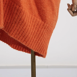 Detail of orange knit sweater showing fine ribbed hem and soft fabric texture